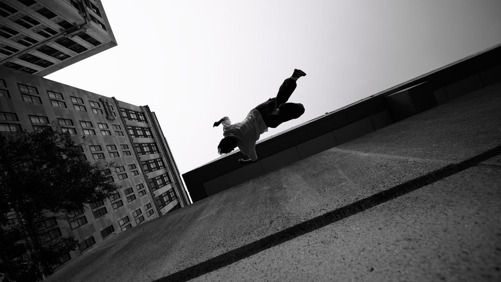 A freerunner vaulting between rooftops, shot from below in black and white.