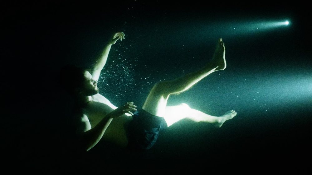 An underwater figure lit by a single beam of teal light.
