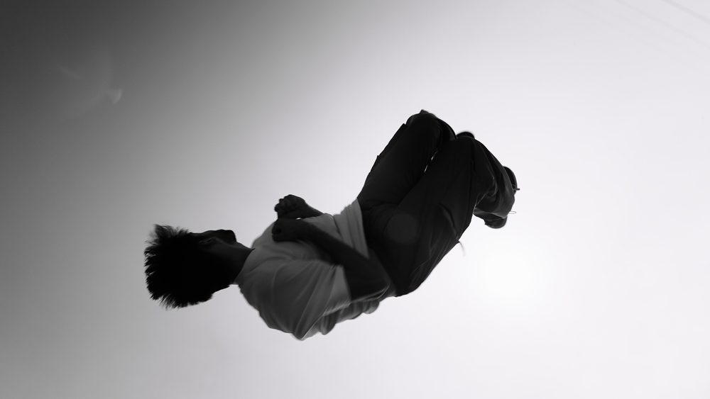 A figure suspended mid-air against a bright empty sky.